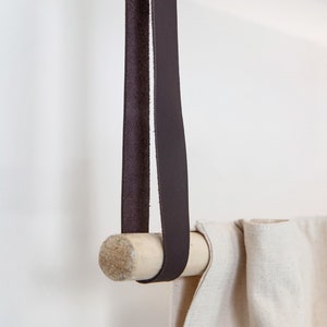 A closeup of a Leather Suspension Strap hanging a curtain with a wooden dowel.