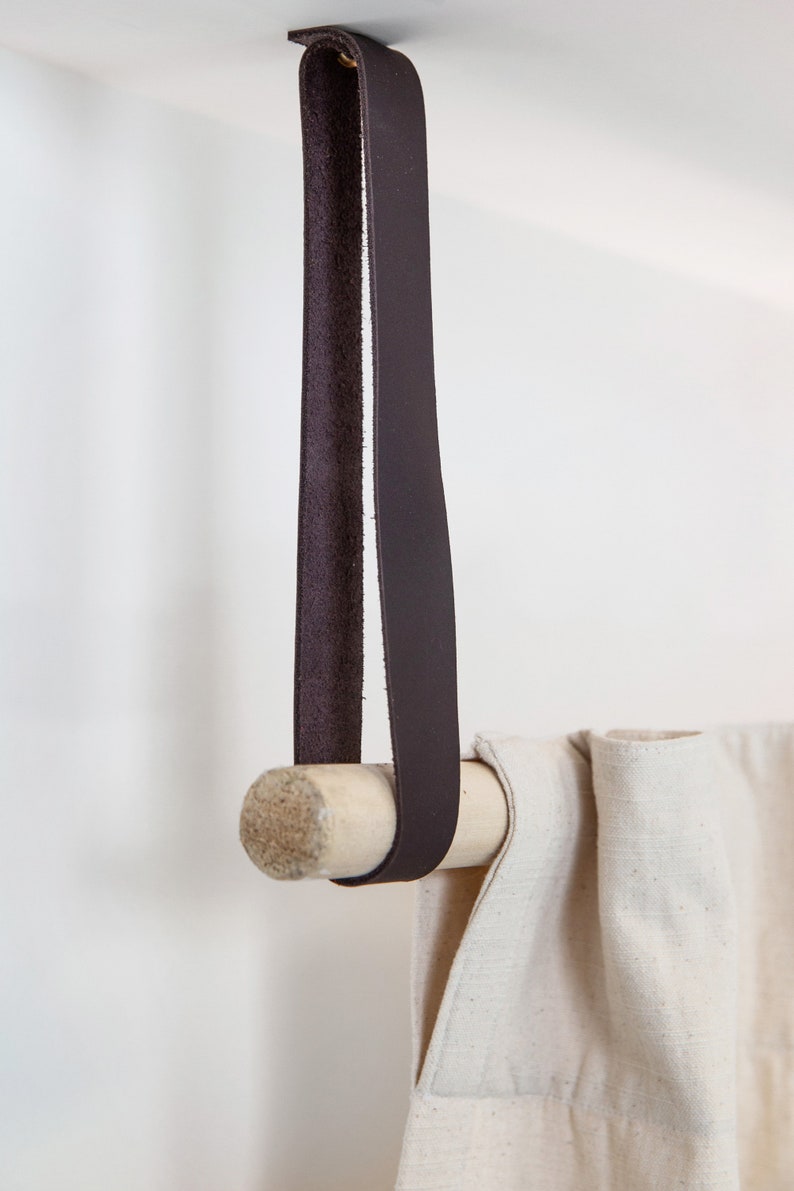 A closeup of a Leather Suspension Strap hanging a curtain with a wooden dowel.