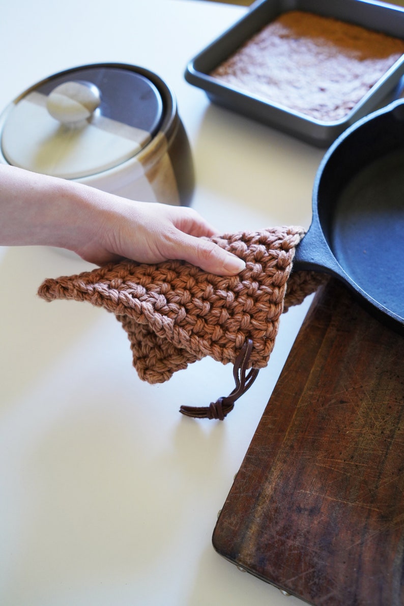 Model holding cast iron pan covering the handle with a pot holder.