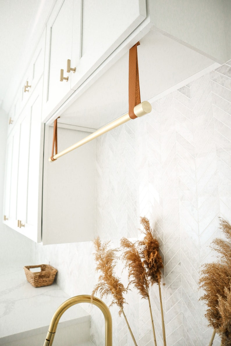 A laundry rack installed with Suspension Straps under a cabinet in a laundry room above a sink.