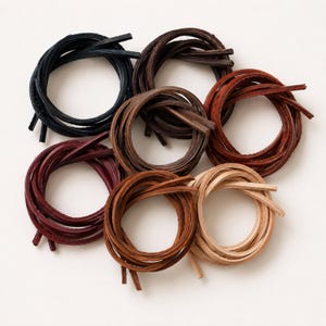 Puede incluir: Un conjunto de cordones de cuero en varios colores, incluyendo negro, marrón y burdeos, dispuestos en haces circulares. Los cordones parecen tener un grosor uniforme y probablemente se utilizan para manualidades o joyería.