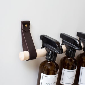 Closeup of a Cabinet Rail Kit installed under the sink on a cabinet door, with spray bottles hung from it.