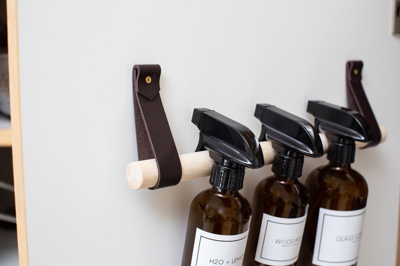 Closeup of a Cabinet Rail Kit installed under the sink on a cabinet door, with spray bottles hung from it.