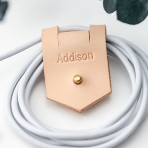 Closeup of Large Leather Cord Holder displayed on a white background wrapped around a cord. Imprinted personalization.