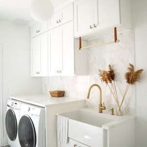 A laundry rack installed with Suspension Straps under a cabinet in a laundry room above a sink.