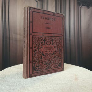 May include: A vintage copy of "Ivanhoe" by Scott, part of the Standard Literature Series. The book has a maroon cover with black lettering and decorative patterns. The spine displays the title and volume number. Published by Newson & Company.