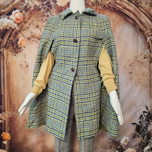 May include: A plaid cape coat featuring a pattern of blue, green, and light blue lines on a textured fabric. The garment has a collared neckline, three dark brown buttons down the front, and arm slits, worn over a mustard yellow long-sleeve shirt.