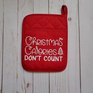 May include: Red quilted pot holder with white text that reads "Christmas Calories Don't Count" and a small white Christmas tree graphic.