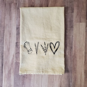May include: A beige kitchen towel with a black design of a salt shaker, two sprigs of herbs, and a heart.