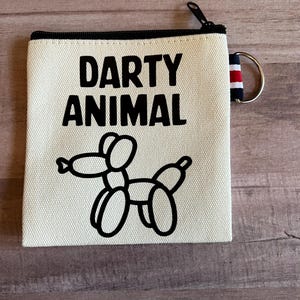 May include: A white canvas zipper pouch with a black zipper and a black and white balloon animal graphic. The pouch has the text "DARTY ANIMAL" printed on it.