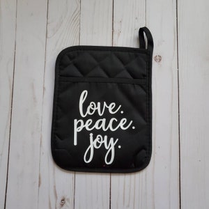 May include: Black quilted oven mitt with a white inscription that reads "love. peace. joy."