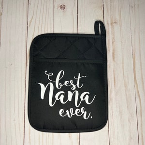 May include: Black quilted oven mitt with the words "best Nana ever" in white script. The mitt has a pocket and a loop for hanging. The background is a light wood grain.