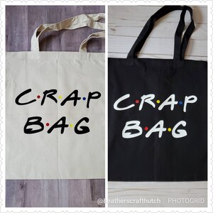 May include: Two tote bags with the text "C.R.A.P. B.A.G." in a white font with colorful dots. One bag is white and the other is black.
