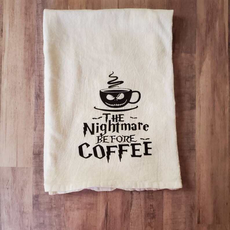 Puede incluir: Una toalla de cocina blanca con un dise&ntilde;o negro de una taza de caf&eacute; con una cara de Jack Skellington y el texto "The Nightmare Before Coffee".