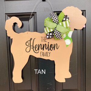 May include: Tan-colored wooden dog silhouette door hanger with a green and black bow. The text "The Hennion Family" is written on the dog's body.