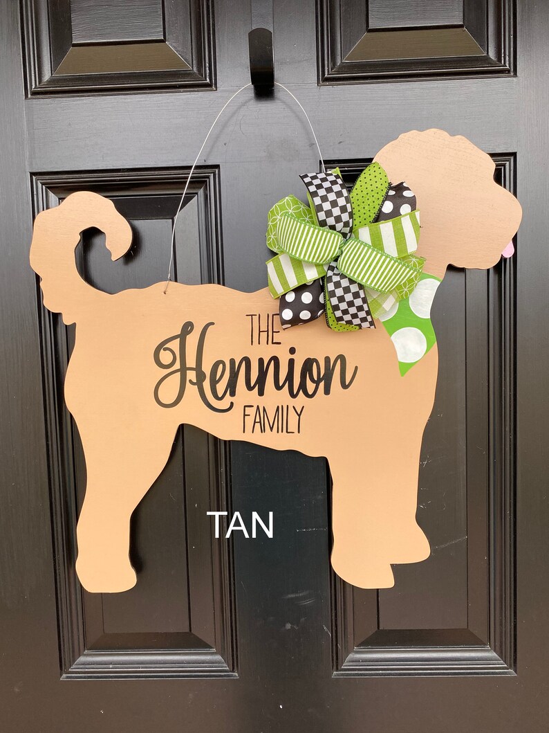 May include: Tan-colored wooden dog silhouette door hanger with a green and black bow. The text "The Hennion Family" is written on the dog's body.