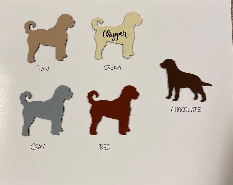 May include: Five dog silhouette cutouts in different colors: tan, cream, chocolate, gray, and red. The cream cutout has the word "Chipper" written on it.