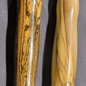 Pode incluir: Dois abre-costuras com cabos de madeira e l&acirc;minas de metal prateado. Uma pega &eacute; castanha escura com riscas pretas, a outra &eacute; castanha clara com riscas castanhas mais escuras. Cada um tem uma bola vermelha na ponta.