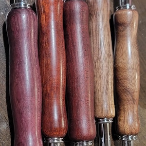 Pode incluir: Cinco rasgadores de costura com cabos de madeira em v&aacute;rios tons de castanho e roxo. Os cabos t&ecirc;m formato ergon&ocirc;mico e s&atilde;o fixados a componentes met&aacute;licos prateados. Cada rasgador tem uma l&acirc;mina afiada com uma bolinha de seguran&ccedil;a vermelha na ponta.