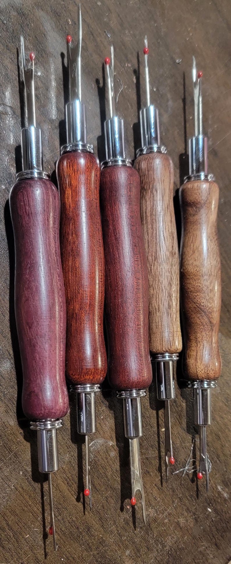 Pode incluir: Cinco rasgadores de costura com cabos de madeira em v&aacute;rios tons de castanho e roxo. Os cabos t&ecirc;m formato ergon&ocirc;mico e s&atilde;o fixados a componentes met&aacute;licos prateados. Cada rasgador tem uma l&acirc;mina afiada com uma bolinha de seguran&ccedil;a vermelha na ponta.