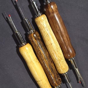 Pode incluir: Quatro rasgadores de costura com cabos de madeira em tons variados de castanho claro e escuro. Cada rasgador tem uma l&acirc;mina de metal prateado e uma bolinha de seguran&ccedil;a vermelha na ponta. Os cabos s&atilde;o lisos e curvos.