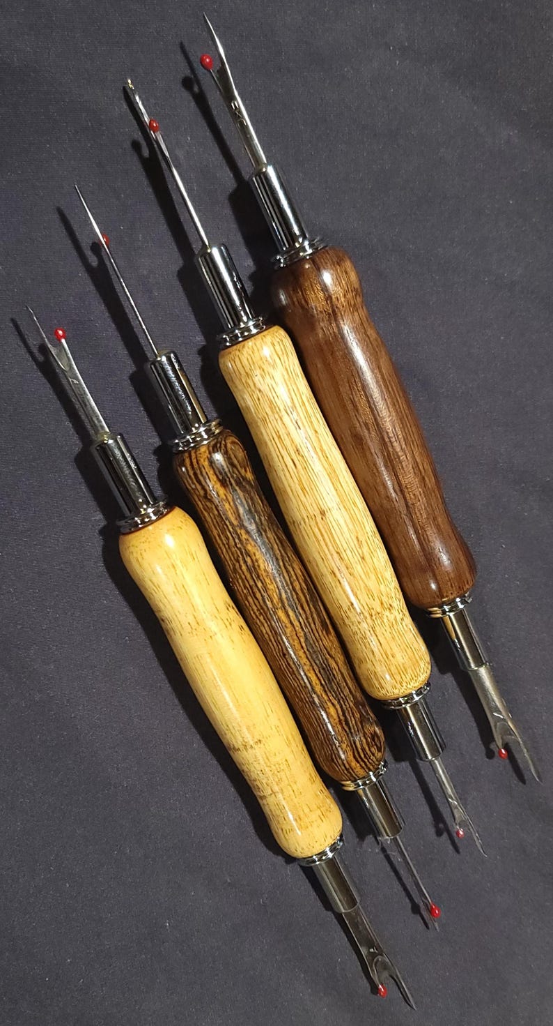 Pode incluir: Quatro rasgadores de costura com cabos de madeira em tons variados de castanho claro e escuro. Cada rasgador tem uma l&acirc;mina de metal prateado e uma bolinha de seguran&ccedil;a vermelha na ponta. Os cabos s&atilde;o lisos e curvos.