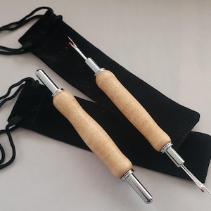Pode incluir: Dois abre costuras com cabos de madeira e detalhes em metal prateado, sobre bolsas pretas de veludo com cord&atilde;o. Os abre costuras t&ecirc;m uma ponta com uma bolinha de seguran&ccedil;a vermelha.