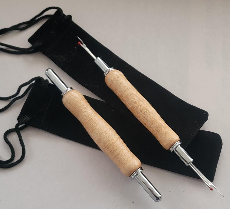Pode incluir: Dois abre costuras com cabos de madeira e detalhes em metal prateado, sobre bolsas pretas de veludo com cord&atilde;o. Os abre costuras t&ecirc;m uma ponta com uma bolinha de seguran&ccedil;a vermelha.