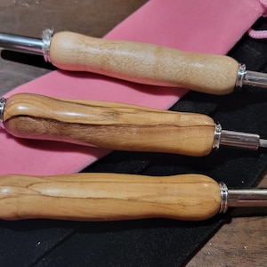 Pode incluir: Tr&ecirc;s rasgadores de costura com cabos de madeira e l&acirc;minas e detalhes em metal prateado. Os cabos t&ecirc;m um acabamento natural de gr&atilde;o de madeira. Os rasgadores de costura est&atilde;o sobre uma bolsa rosa e uma bolsa preta com cord&atilde;o.