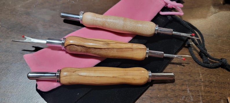 Pode incluir: Tr&ecirc;s rasgadores de costura com cabos de madeira e l&acirc;minas e detalhes em metal prateado. Os cabos t&ecirc;m um acabamento natural de gr&atilde;o de madeira. Os rasgadores de costura est&atilde;o sobre uma bolsa rosa e uma bolsa preta com cord&atilde;o.