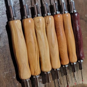 Pode incluir: Uma cole&ccedil;&atilde;o de desfibradores com cabos de madeira em v&aacute;rios tons de castanho claro e bord&ocirc; escuro. Os desfibradores t&ecirc;m l&acirc;minas de metal prateado e pontas vermelhas, ideais para projetos de costura e artesanato.