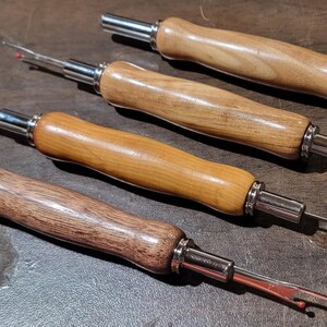 Pode incluir: Quatro rasgadores de costura com cabos de madeira e componentes de metal prateado. Os cabos variam em cor, do castanho claro ao escuro. Cada rasgador tem uma l&acirc;mina afiada com ponta vermelha.