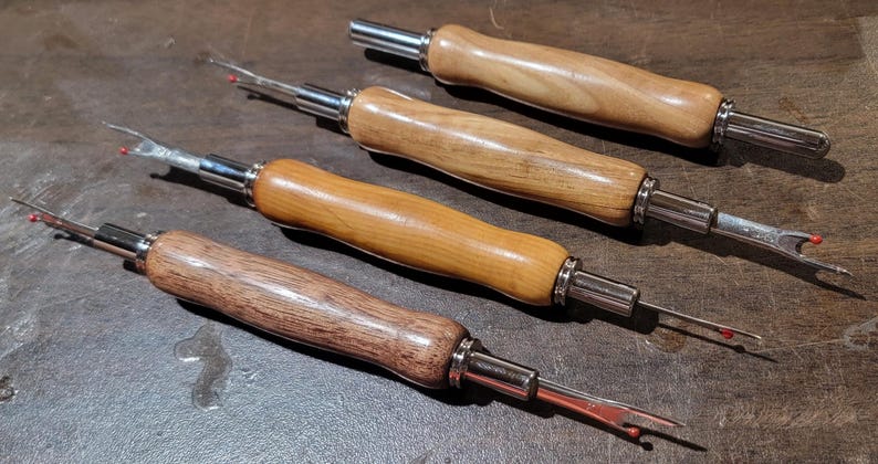 Pode incluir: Quatro rasgadores de costura com cabos de madeira e componentes de metal prateado. Os cabos variam em cor, do castanho claro ao escuro. Cada rasgador tem uma l&acirc;mina afiada com ponta vermelha.
