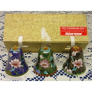 May include: A set of three cloisonné bells in blue, green, and black, each featuring a floral pattern with pink petals and gold-tone rims. The bells are displayed in front of a rectangular gold box with a red label reading 3807 CLOISONNE BELL SET/3.