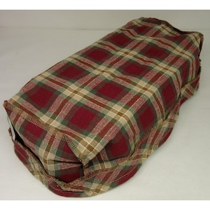 May include: A rectangular fabric cushion featuring a woven plaid pattern in shades of deep red, forest green, and tan. The item has visible stitched seams along the edges and a textured, woven appearance throughout the entire surface of the textile.