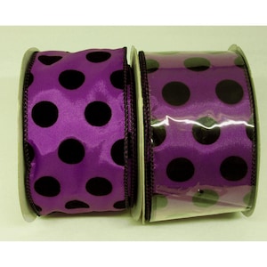 May include: Two rolls of purple ribbon with large black polka dots. The ribbon is made of a shiny fabric and has a wired edge. The rolls are side-by-side, with one partially unwound, revealing the pattern.