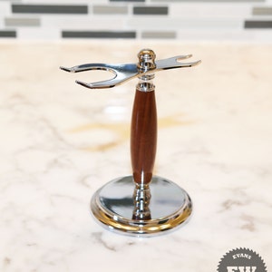 Puede incluir: Un soporte para brocha de afeitar de cromo y madera. El soporte tiene una base circular y un mango de madera marrón oscuro. La parte superior del soporte tiene un soporte cromado para una brocha de afeitar. El soporte está diseñado para sujetar una brocha de afeitar y una maquinilla.