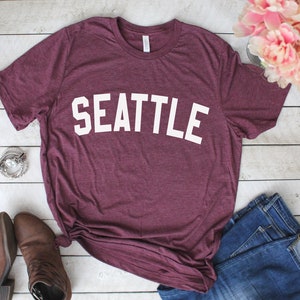 May include: A maroon t-shirt with the word "SEATTLE" printed in white on the front.