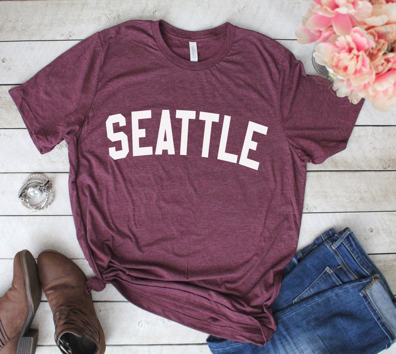 May include: A maroon t-shirt with the word "SEATTLE" printed in white on the front.