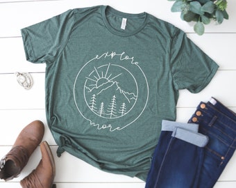 May include: A green t-shirt with a white graphic of a mountain range, sun, and trees in a circle with the text "explore more".