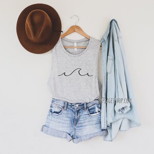 May include: A gray tank top with a simple black wave design. The tank top is styled with denim shorts and a light blue denim jacket.