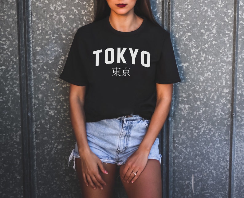 K&ouml;nnte beinhalten: Ein schwarzes T-Shirt mit wei&szlig;em Text, auf dem "TOKYO" und "東京" in japanischen Schriftzeichen steht.