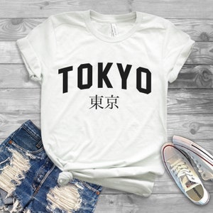 K&ouml;nnte beinhalten: Wei&szlig;es T-Shirt mit schwarzem Text, auf dem "TOKYO" und "東京" in japanischer Sprache steht.