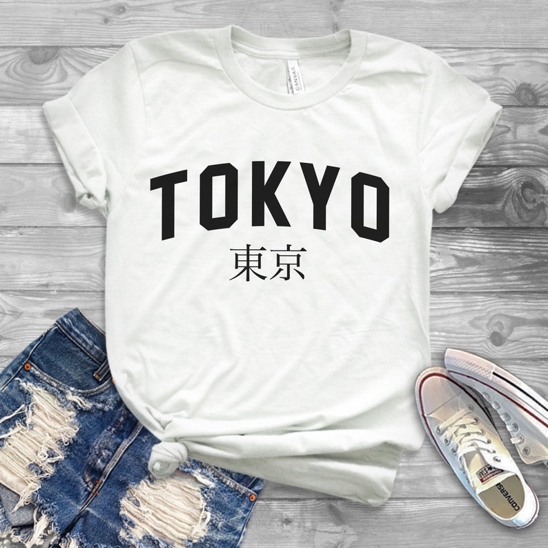 K&ouml;nnte beinhalten: Wei&szlig;es T-Shirt mit schwarzem Text, auf dem "TOKYO" und "東京" in japanischer Sprache steht.