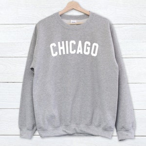 Puede incluir: Una sudadera gris con la palabra "CHICAGO" impresa en blanco en la parte delantera.