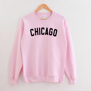 Puede incluir: Una sudadera rosa con la palabra "CHICAGO" impresa en negro en la parte delantera.