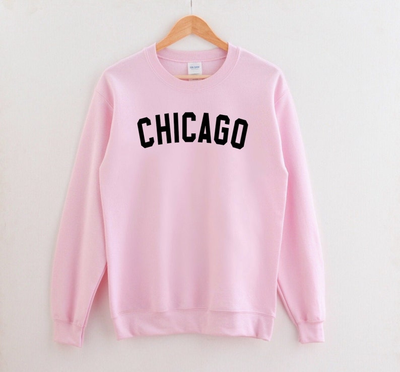 Puede incluir: Una sudadera rosa con la palabra "CHICAGO" impresa en negro en la parte delantera.