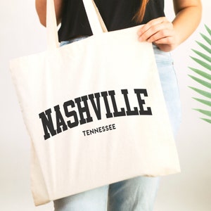 May include: A white canvas tote bag with black handles and the text "NASHVILLE TENNESSEE" printed in black.
