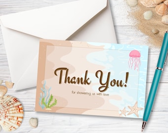 Puede incluir: Una tarjeta de agradecimiento con temática de playa con las palabras "Thank You!" en escritura marrón. La tarjeta presenta ilustraciones de una medusa, estrellas de mar y algas marinas. También hay un sobre blanco y un bolígrafo turquesa.