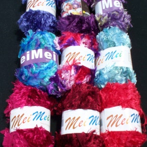 May include: Eight spools of fuzzy yarn in various colors, including purple, blue, pink, and red. Each spool has a white label with the text "Mei Mei" printed on it.